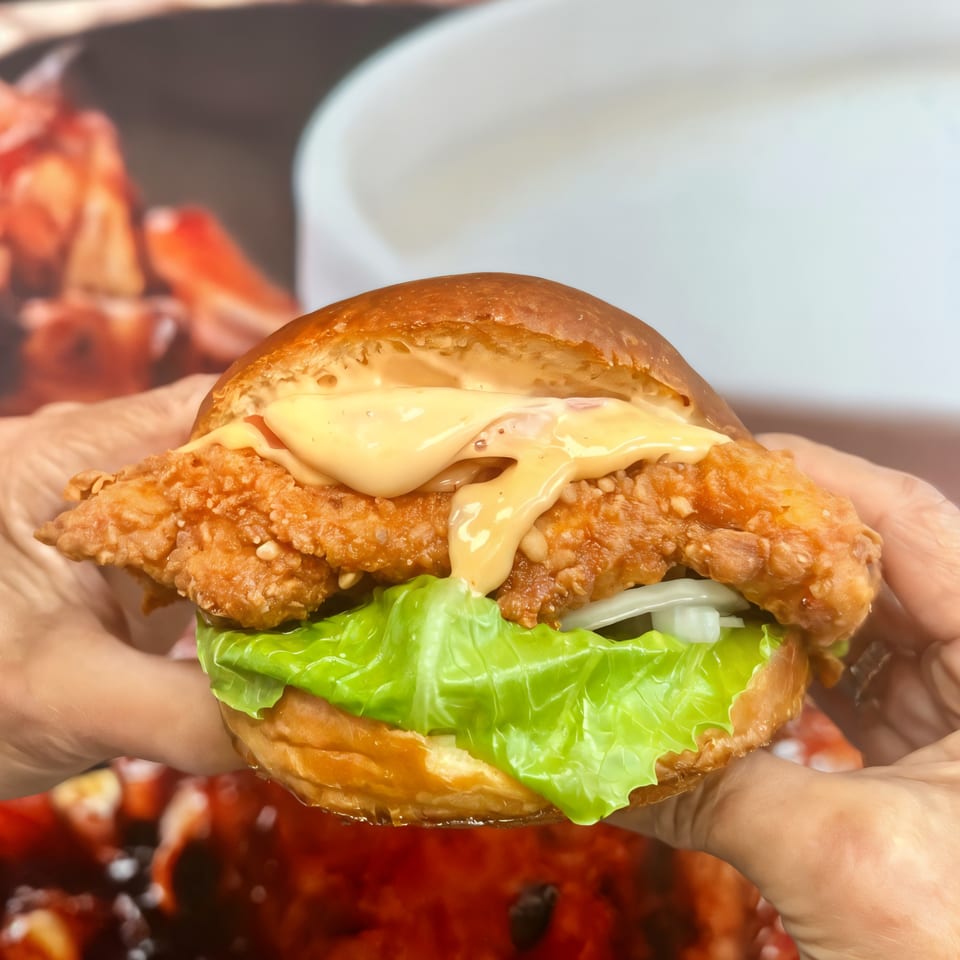 Hands holding a Smashbros Halal Grill fried chicken sandwich with sauce, lettuce, and onions.