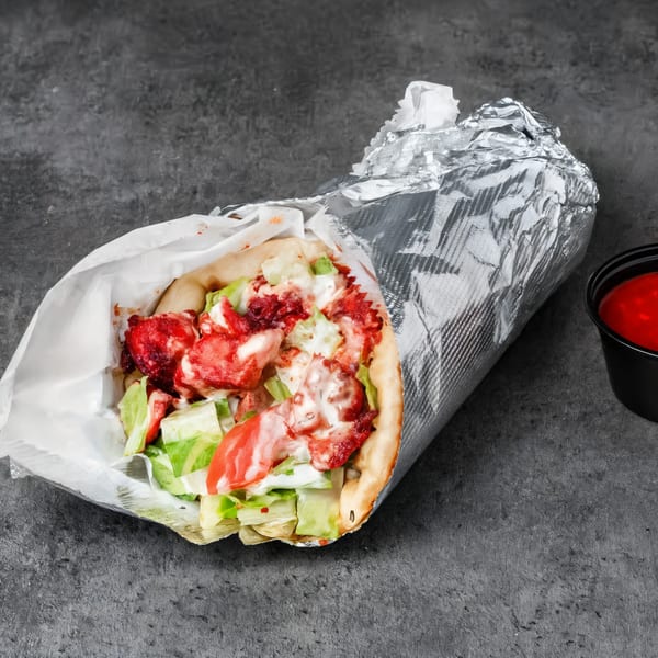 Halal chicken gyro with red sauce, white sauce, lettuce, and tomatoes, wrapped in foil.