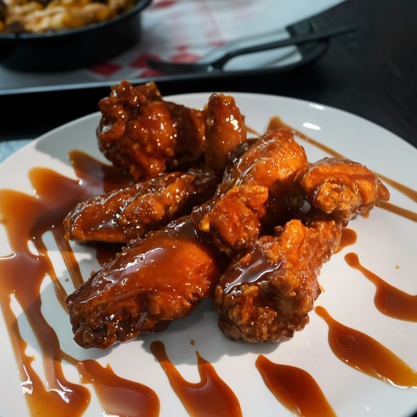 A white plate holds several golden-brown chicken wings generously coated in a glossy, dark orange sauce.