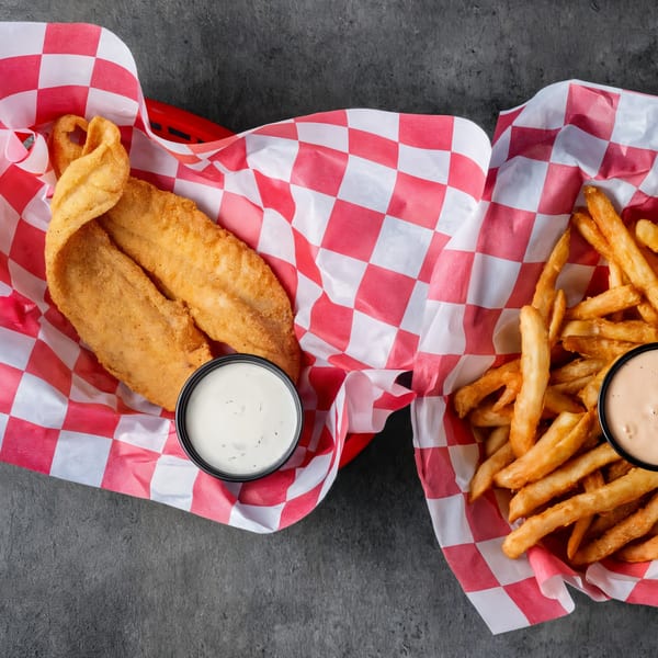 Two baskets of fried fish and french fries with dipping sauces on a dark surface.