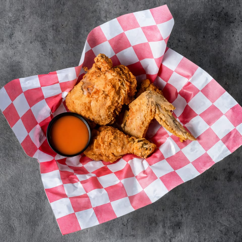 Crispy fried halal chicken pieces and a dipping sauce in a red and white checkered basket liner.