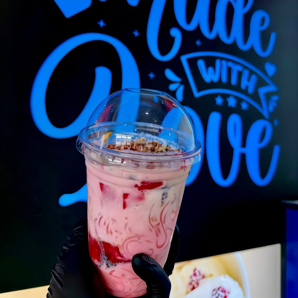 Hand in black glove holding a pink drink with red and black toppings, against a blue neon sign.