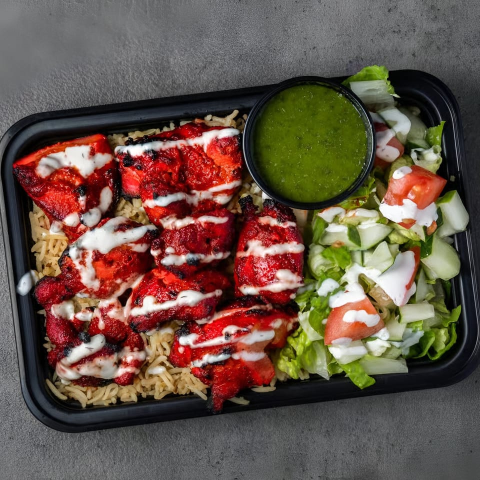 Halal grilled chicken tikka over rice, with a side salad and green chutney in a black container.