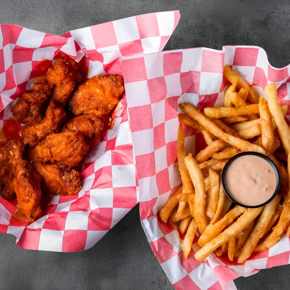 Halal chicken wings and french fries with dipping sauce in red and white checkered baskets.
