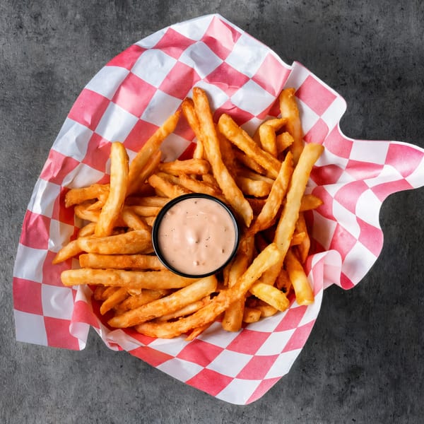 Golden french fries in a red and white checkered paper basket with a side of dipping sauce.