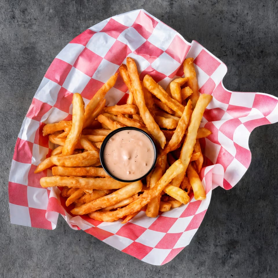 Golden french fries in a red and white checkered paper basket with a side of dipping sauce.